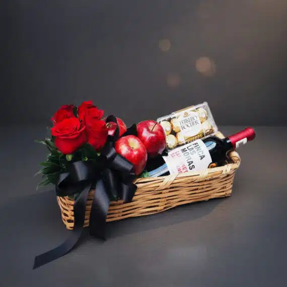 Arreglo ANGELO: Elegante cesta de mimbre con rosas rojas frescas, manzanas rojas, botella de vino tinto Finca Las Moras y caj