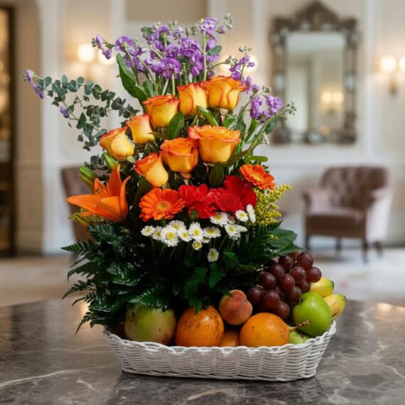 Arreglo floral Hadar con rosas naranjas, lirios, gerberas y margaritas, acompañado de frutas frescas como uvas, manzanas, nar