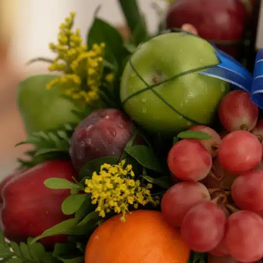 Primer plano extremo de un Arreglo Floral Gourmet ITALINA con frutas exóticas, uvas rojas, manzanas verdes, ciruelas y una ma