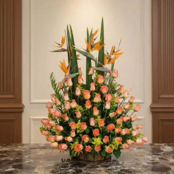 Arreglo Floral Más Rosas: Elegancia con Aves del Paraíso Arreglo floral grande con rosas color salmón y aves del paraíso, sobre una mesa de mármol en un entorno elegante de hotel bou