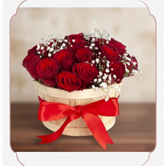 Arreglo floral 'Lidia' con 15 rosas rojas premium en un balde rústico de madera, adornado con un lazo rojo y follaje blanco,