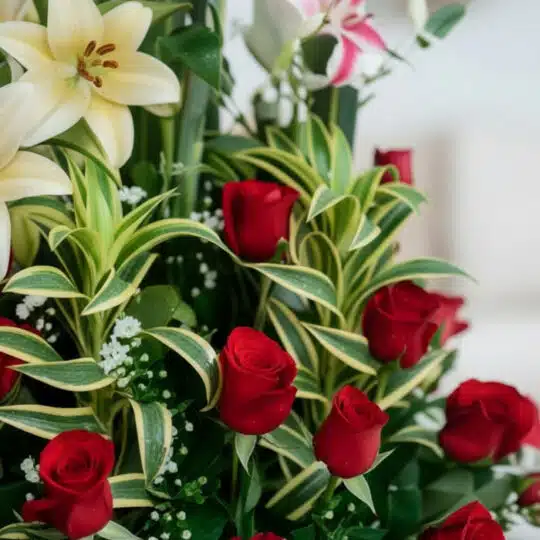 Primer plano extremo de un arreglo floral 'Siempre Juntos' con lirios blancos, rosas rojas frescas y follaje verde, destacand