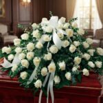 Arreglo fúnebre cubre caja Misericordia con rosas blancas frescas y follaje verde, presentado en una sala de velación premium