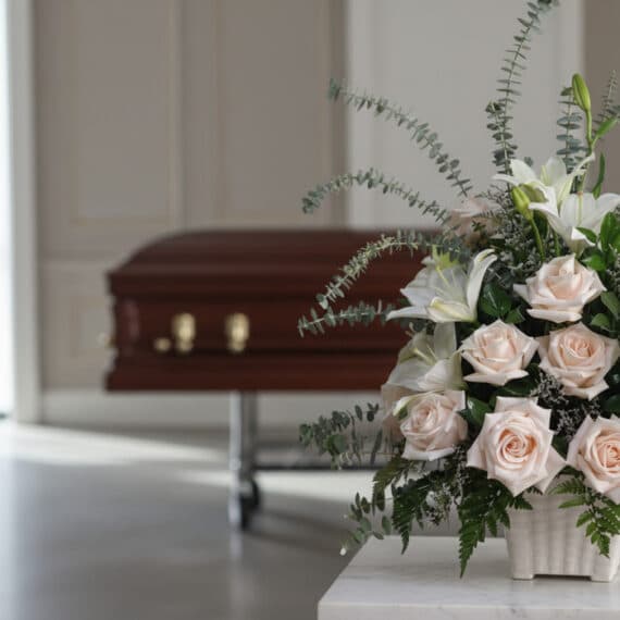 Arreglo floral fúnebre Inmortal con rosas pálidas, lirios blancos y eucalipto, en primer plano en una sala de velación modern
