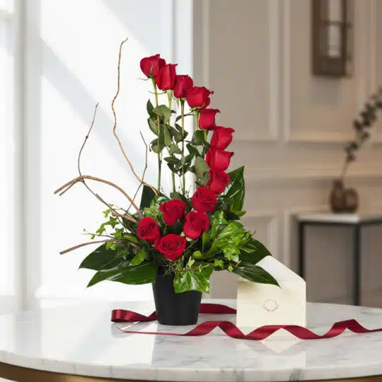 Arreglo floral GIANNA con 13 rosas rojas en jarrón negro, tarjeta de regalo y cinta satinada sobre mesa de mármol. Ideal para