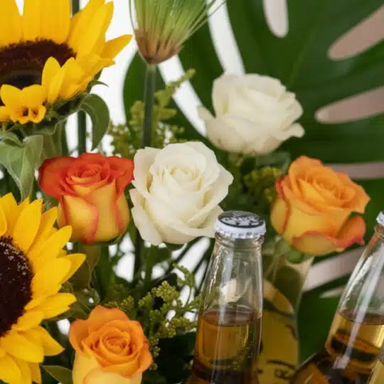 Primer plano extremo de Arreglo con Girasoles Temis, mostrando girasoles, rosas blancas y naranjas, y botellas de cerveza con
