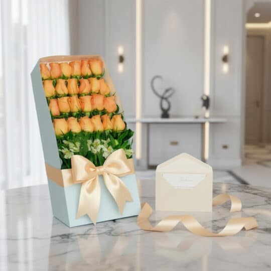 Caja de 24 rosas salmón frescas en empaque azul con lazo satinado, tarjeta de regalo y cinta sobre mármol.