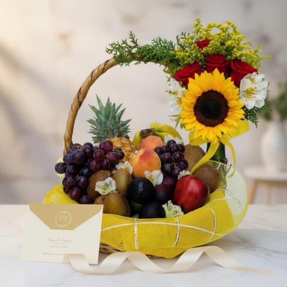 Canasta de Frutas Draco con piña, uvas, kiwis, duraznos, manzanas y ciruelas, decorada con girasol, rosas rojas y alstroemeri