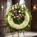 Corona fúnebre "Legado de Hildegarda" con rosas blancas y rojas, crisantemos blancos y follaje verde, en sala de velación pre