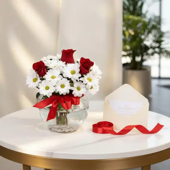 Jarron Floral Antonietta con rosas rojas y margaritas blancas, lazo rojo, tarjeta de regalo en sobre y cinta satinada sobre m