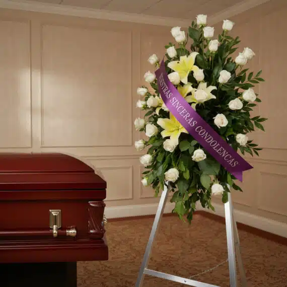 Pedestal fúnebre "Luz de Jacinta" con rosas blancas y lirios amarillos, cinta morada con mensaje de condolencia, junto a un a