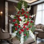 Pedestal fúnebre Homenaje con rosas rojas, lirios blancos y gladiolos, en una sala de velación premium con luz natural suave.