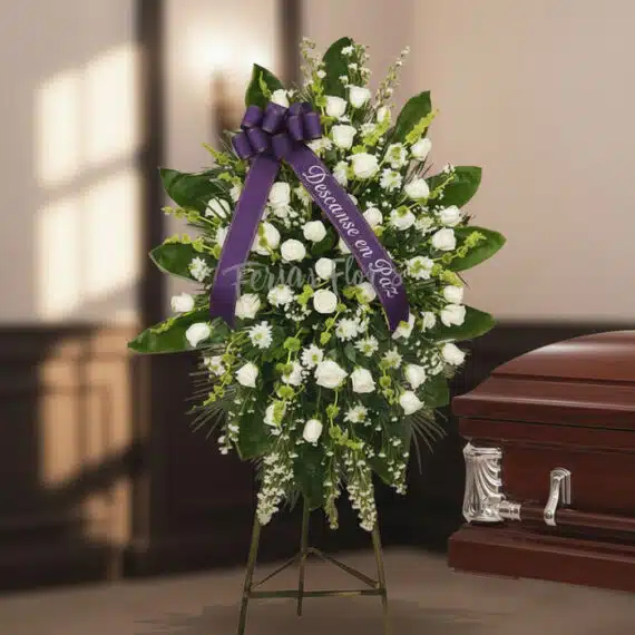 Pedestal fúnebre "Nunca te Olvidaré" con rosas blancas y follaje verde, cinta morada con mensaje de condolencia, junto a un a