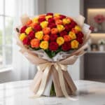 Impresionante ramo SYLVANA con 60 rosas rojas, naranjas y amarillas vibrantes, envuelto en papel coreano beige y atado con un