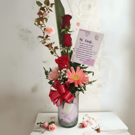 Arreglo floral Solitario Pienso en Ti con rosas rojas, gerberas y follaje en un jarrón de cristal, sobre un fondo elegante de